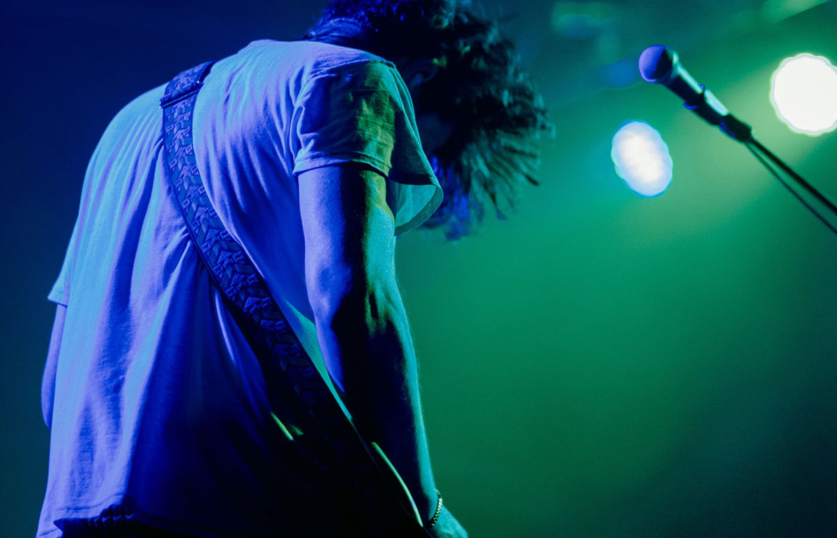 Musician on stage with guitar strap and microphone under blue and green stage lighting